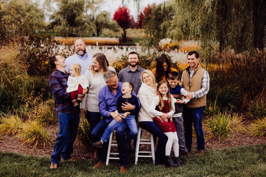 Joyful extended family moment in Sheboygan, WI with grandparents holding grandchildren while the whole family laughs together in autumn setting.