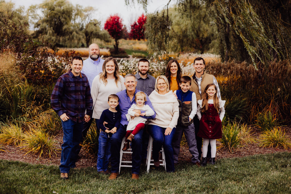 Formal Roe family portrait in Sheboygan, WI with grandparents, adult children, and grandchildren gathered in front of vibrant fall foliage.