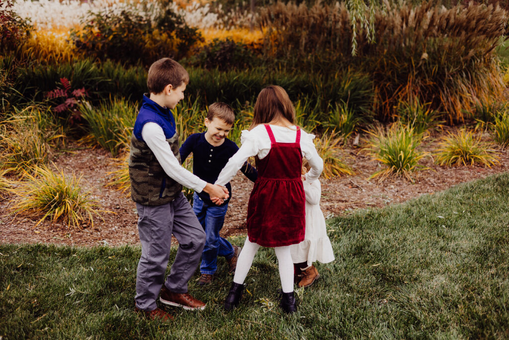 Four cousins laughing and spinning in a circle outdoors during extended family photography session in Sheboygan, Wisconsin.