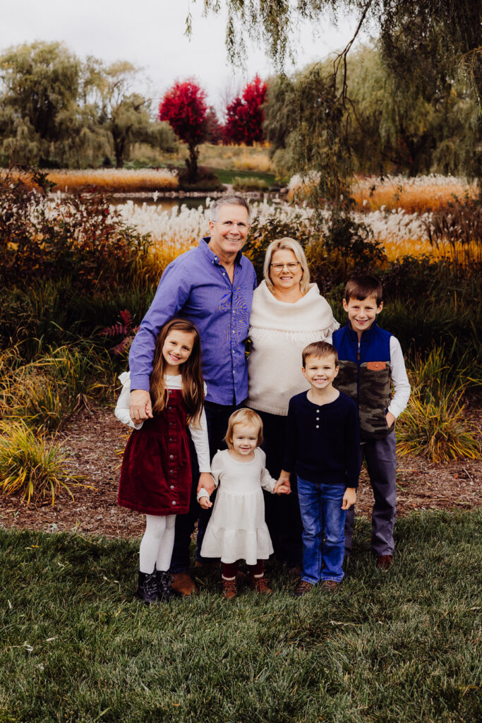 Grandparents smiling with their four grandchildren in front of autumn trees and golden grasses during Sheboygan family photo session.