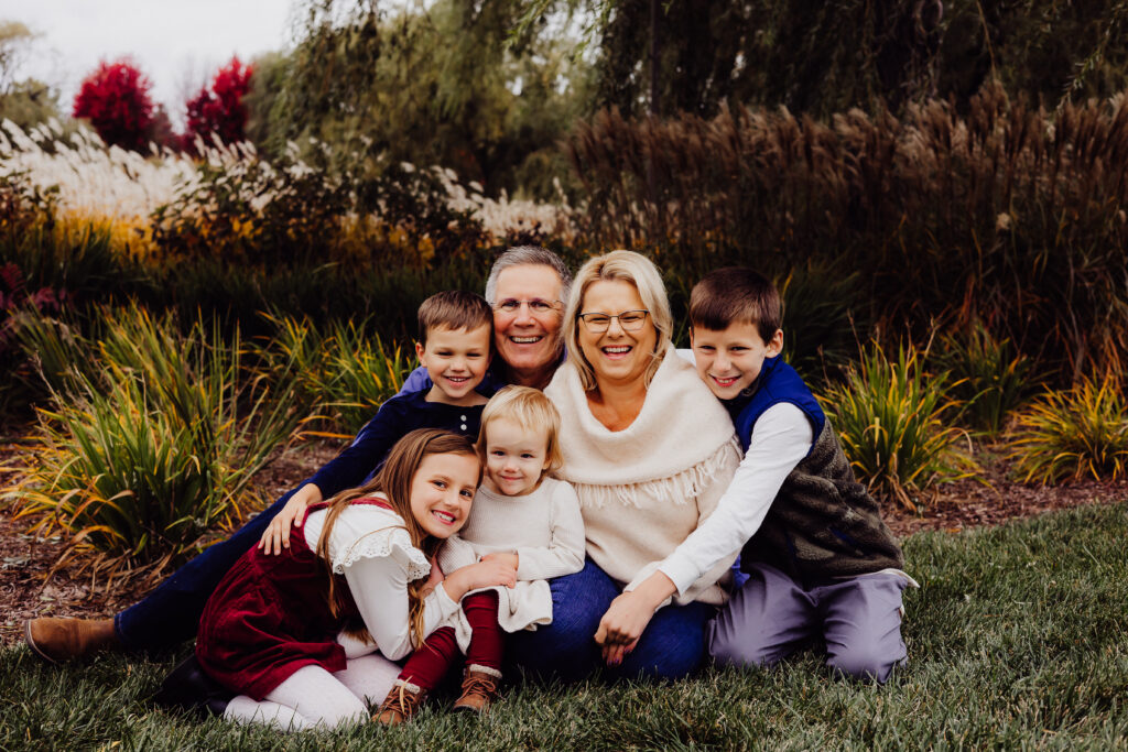 Grandparents sitting on the grass surrounded by their four smiling grandchildren during a fall family photo session in Sheboygan, WI.