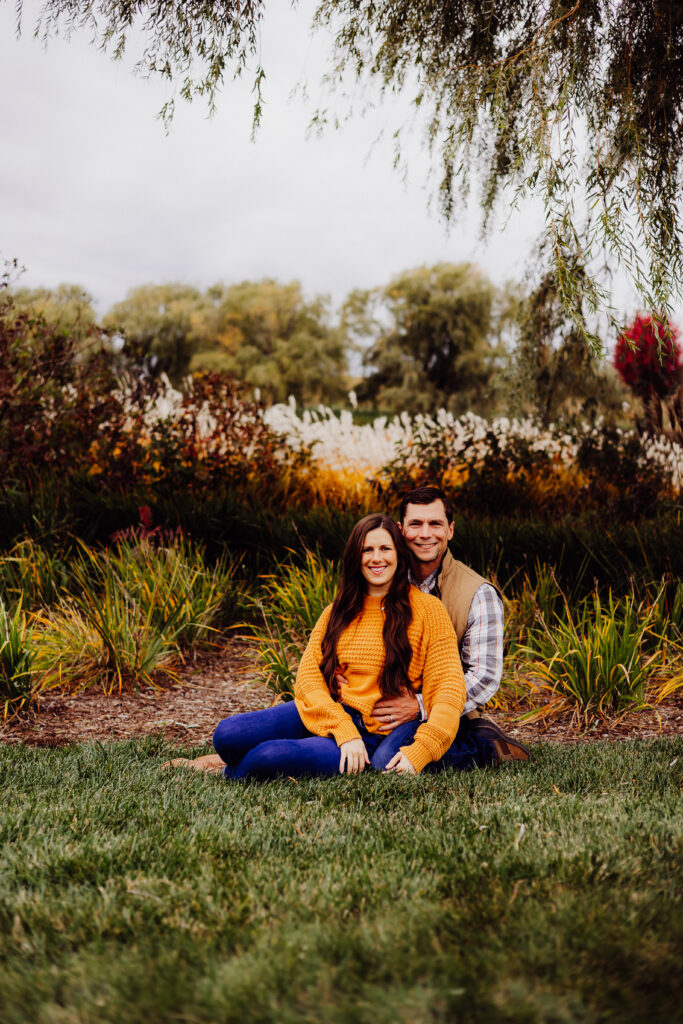 Husband and wife sitting close together on the grass during a fall family photo session in Sheboygan, Wisconsin.