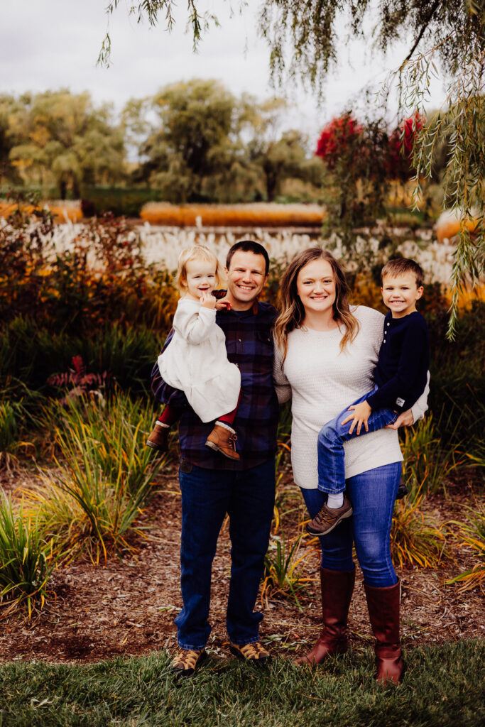 Parents holding two young children and smiling outdoors during fall family session in Sheboygan, WI.