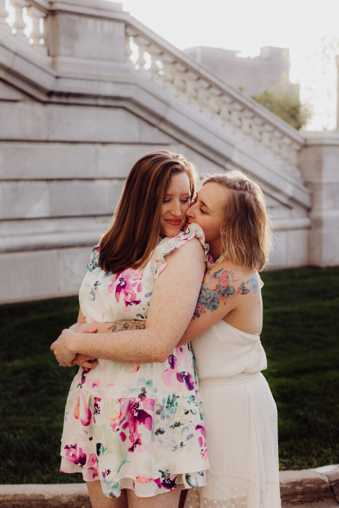 Lauren smiling while Carley kisses her shoulder during their romantic spring engagement photos at the Wisconsin State Capitol.