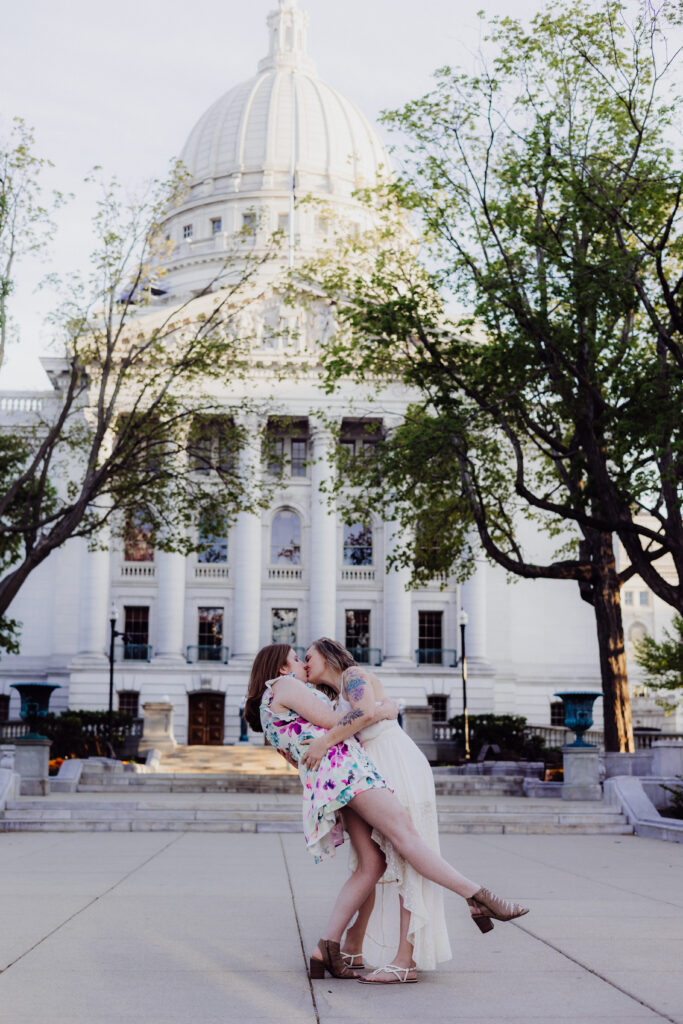 Carley playfully dipping Lauren for a kiss in front of the Wisconsin State Capitol during their spring engagement session in Madison, WI.