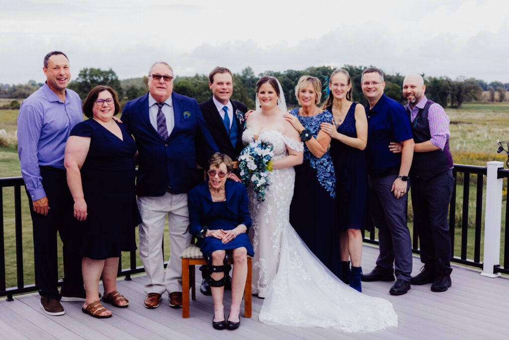 Bride and groom pose with extended family on outdoor deck overlooking fields during Juneau, Wisconsin barn wedding.